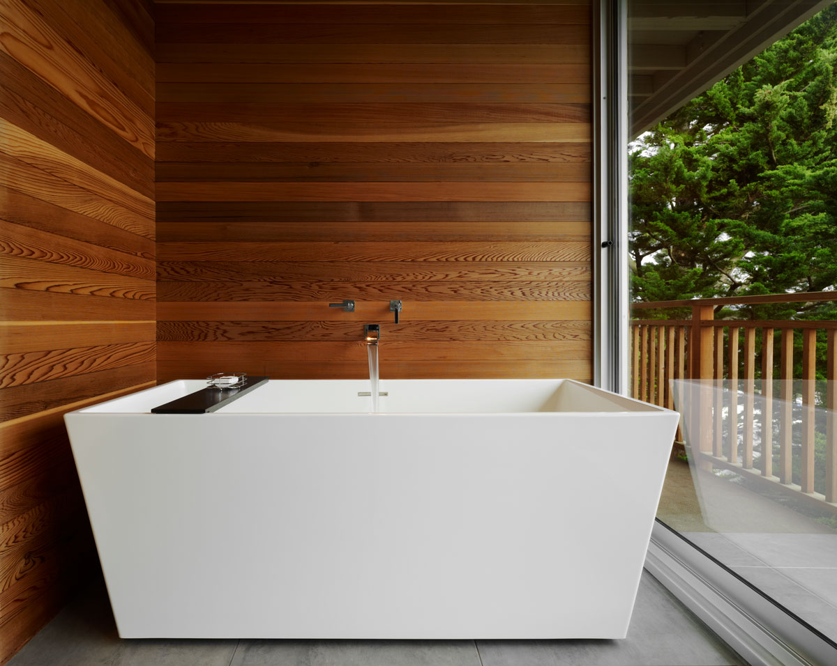 White freestanding bathtub with wooden walls with glass doors and deck access
