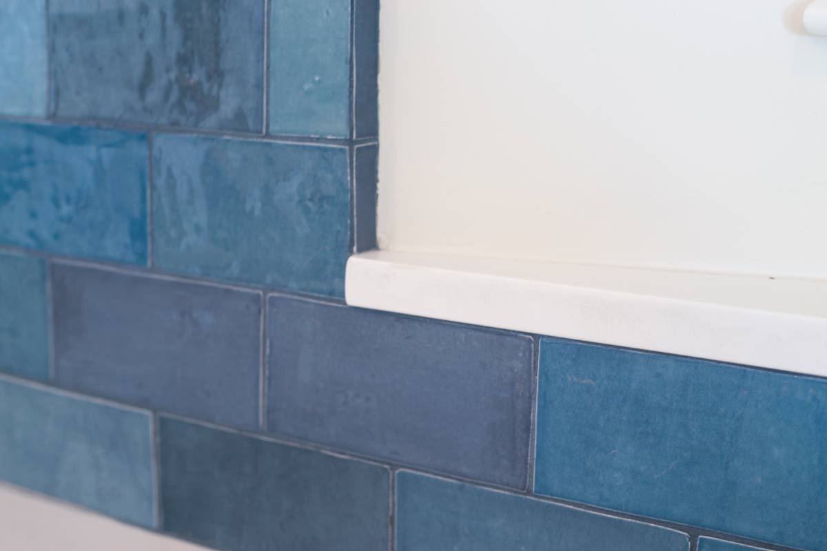 Close-up of a wall displaying rectangular blue tiles in varying shades. Adjacent is a white surface, creating a contrast with the tile pattern.