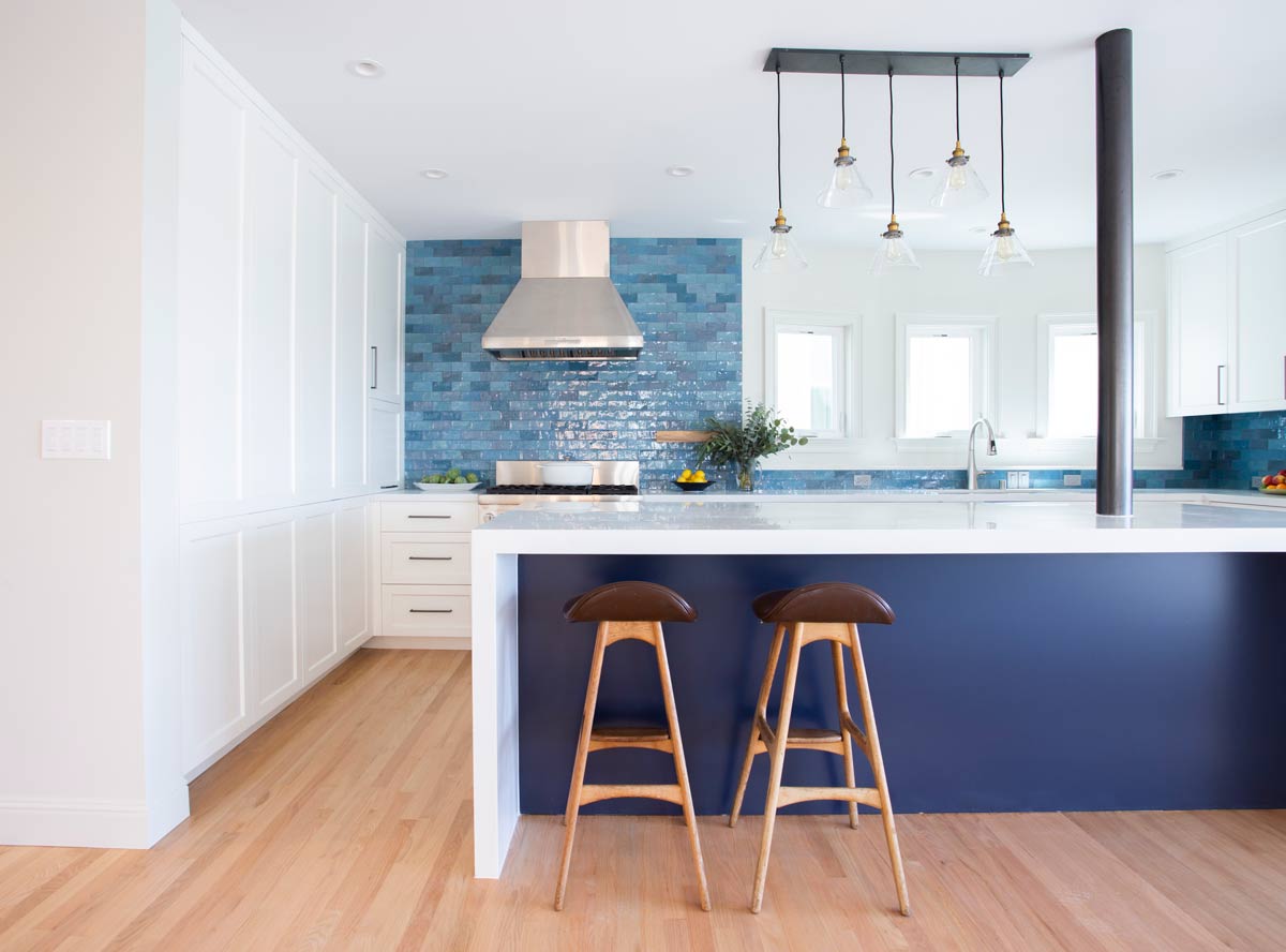 Modern kitchen remodel in San Francisco with white cabinets, blue tiled backsplash, and wooden flooring. Features a sleek island with two wooden barstools, pendant lights, and stainless steel appliances. Natural light from windows brightens the space.